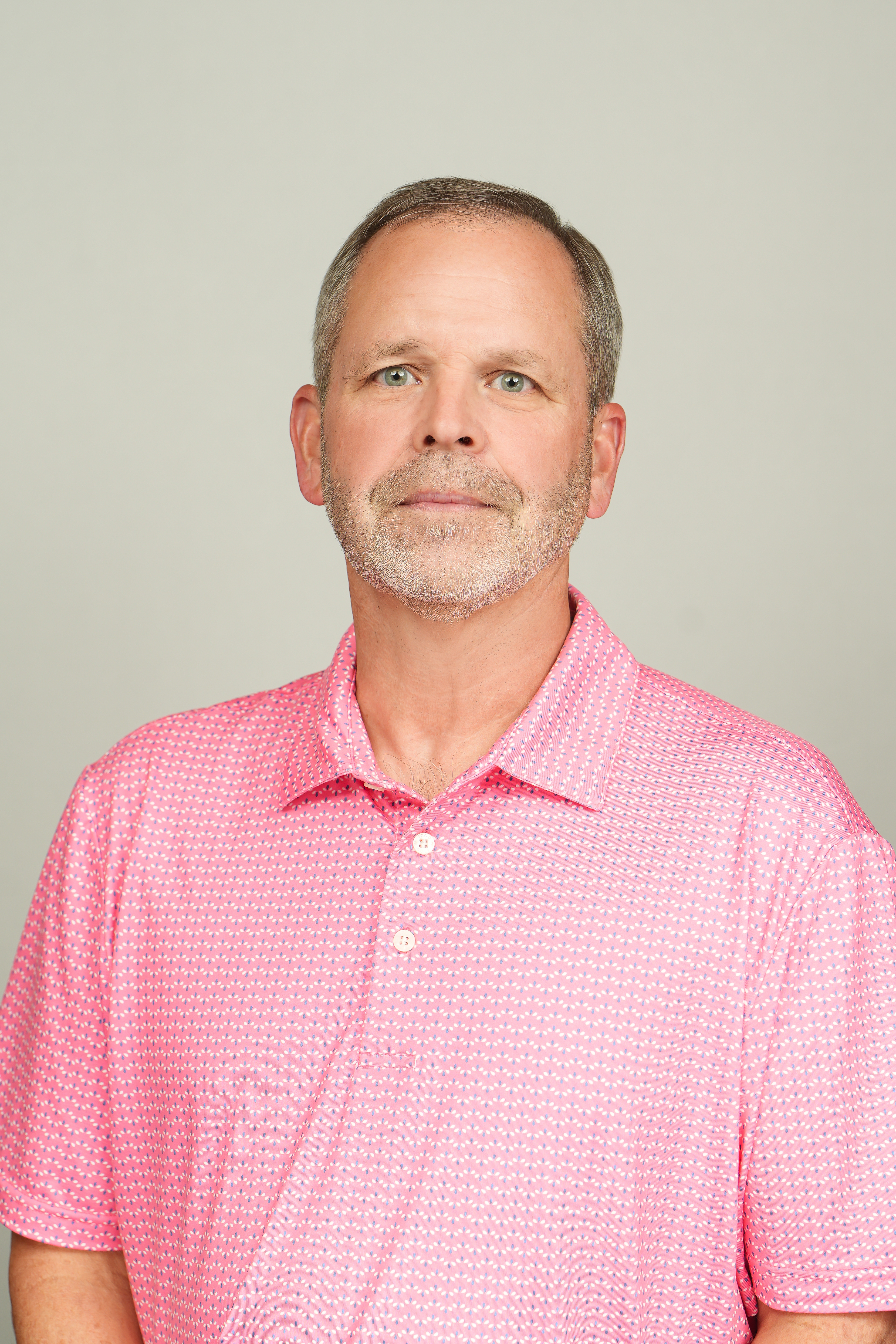 Professional headshot of a person with short gray hair and a trimmed beard, wearing a pink patterned polo shirt.